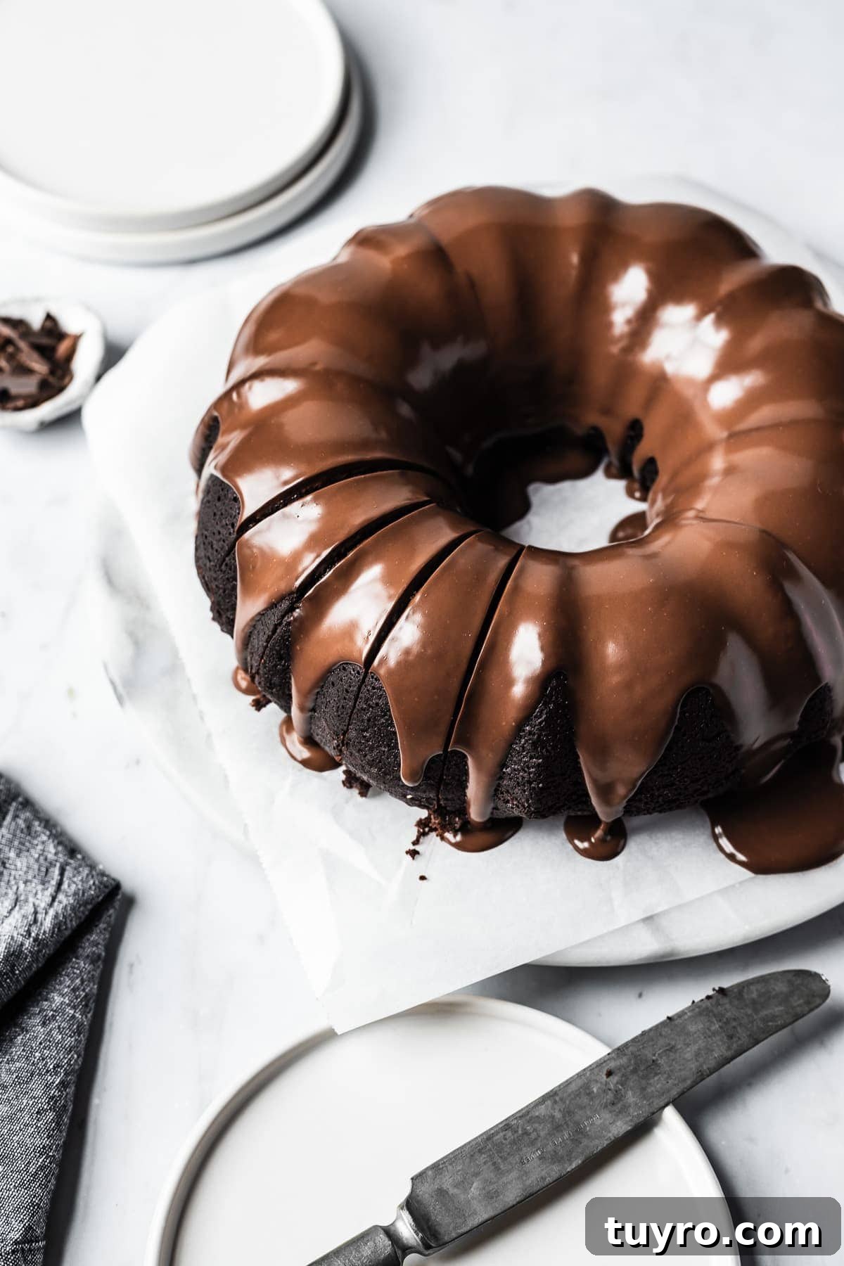 Close up of sliced chocolate olive oil bundt cake with chocolate ganache glaze on a white marble platter