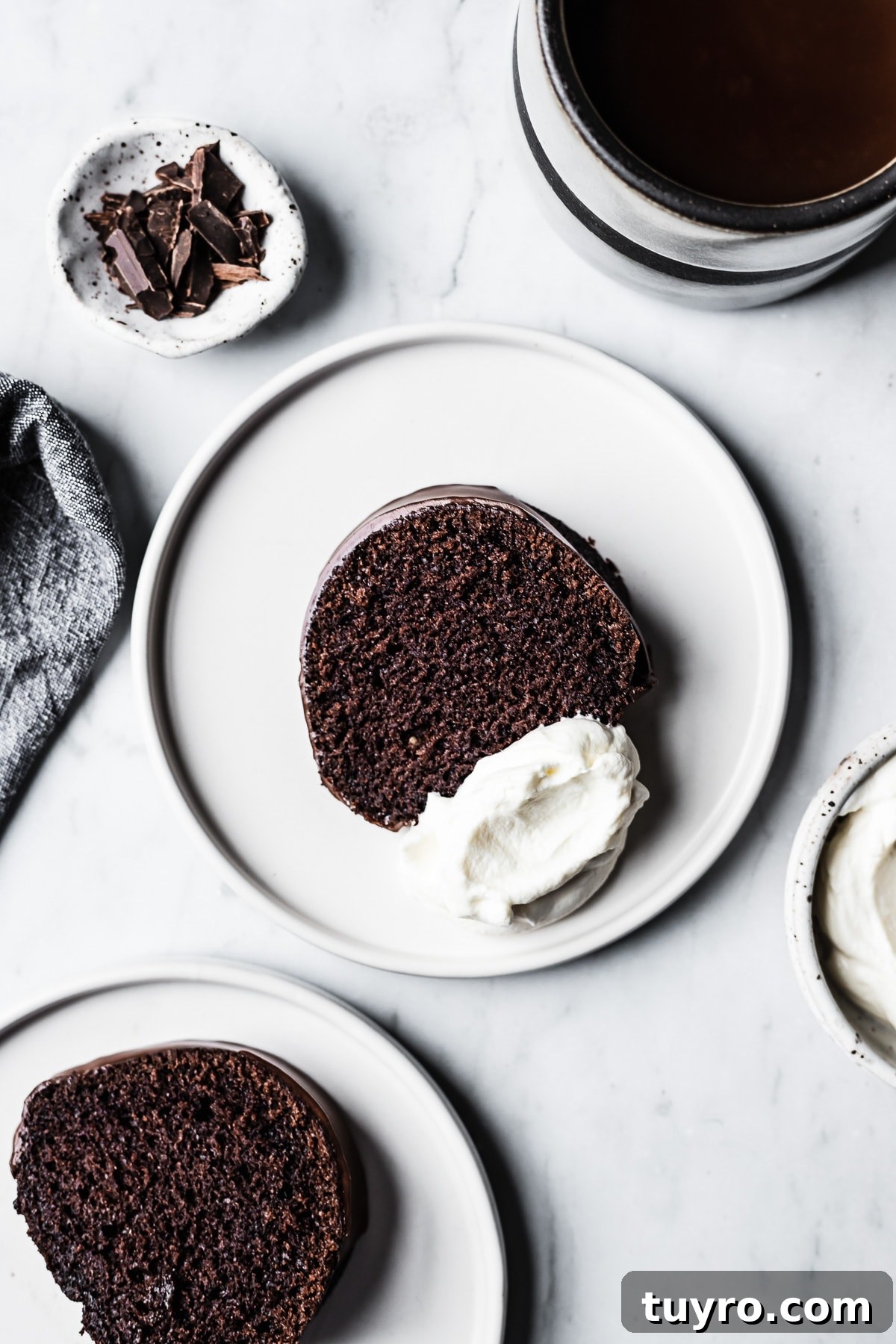 Slices of chocolate bundt cake on white plates with coffee, whipped cream and napkin resting nearby