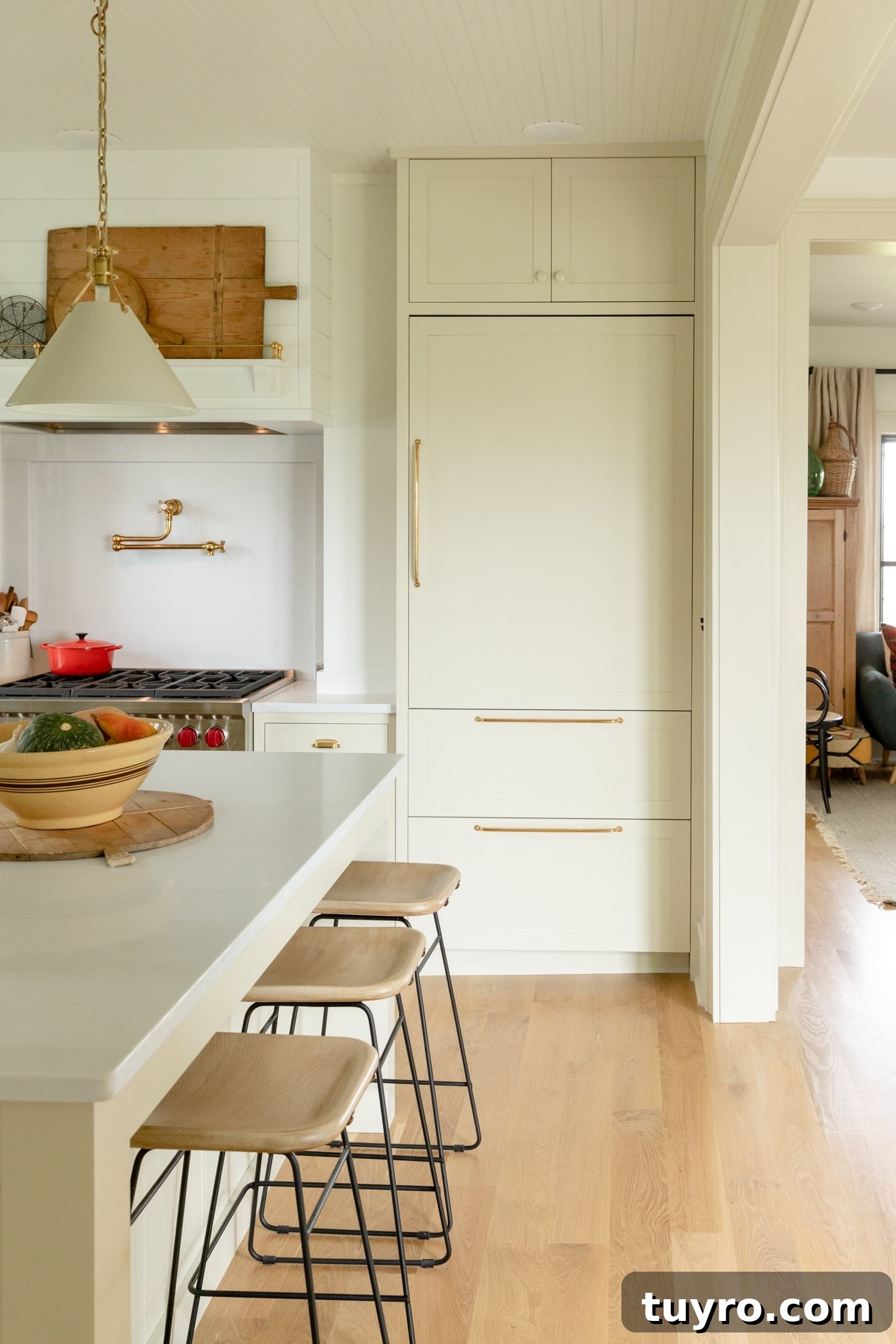 Large panel front refrigerator sitting behind island with stools and light hardwood floors