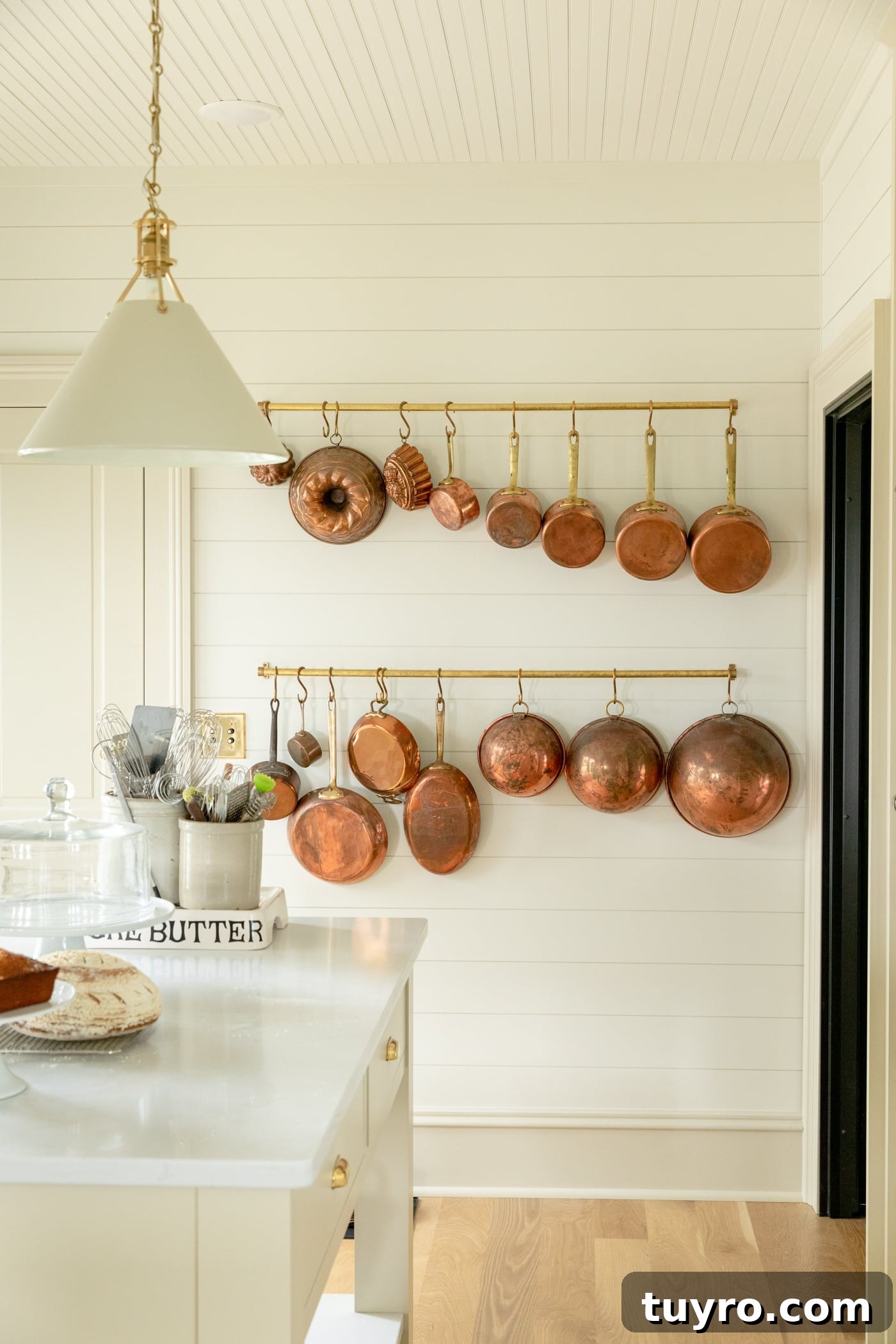 Lots of copper pots hanging on a brass rail with ship lap and large baseboard all with light wood floors