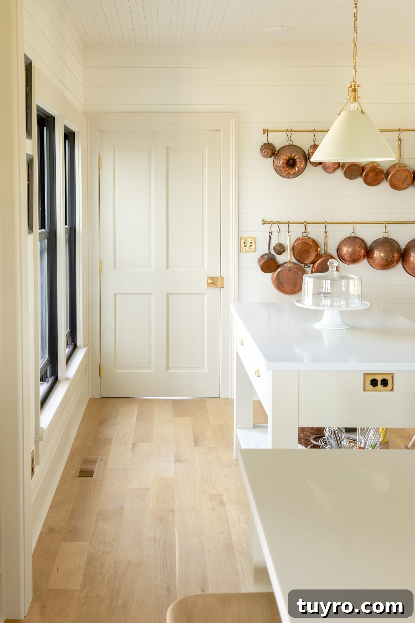Four square creamy colored panel door with light oak floors leading up to it with small island to the side