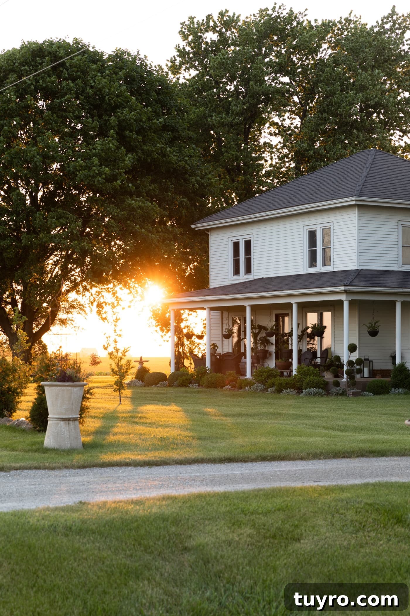 Exterior of white farmhouse with large front door and double windows with sun setting in background
