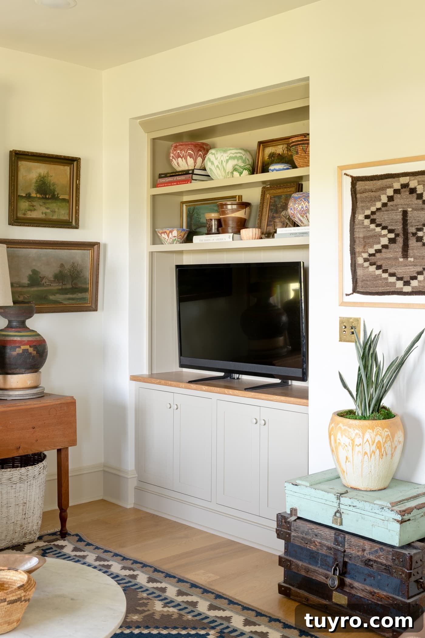 TV sitting in a built-in unit with cabinets underneath and shelves above with paintings on the surrounding walls and a blue rug on on the hardwood floors