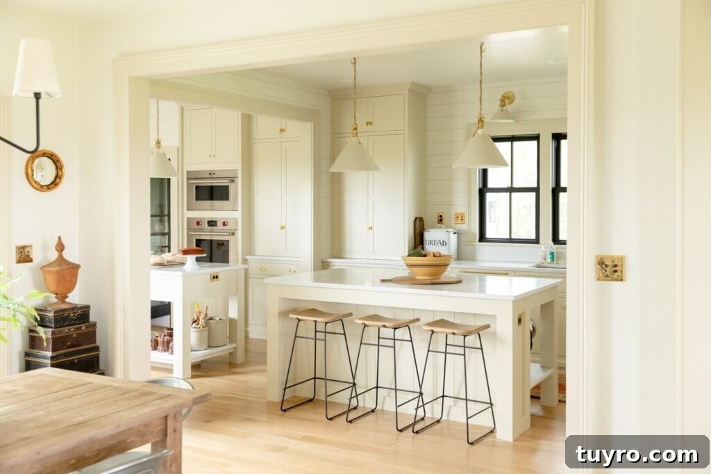 Creamy and light farmhouse kitchen with large island and three stool tucked away with wall oven and black windows