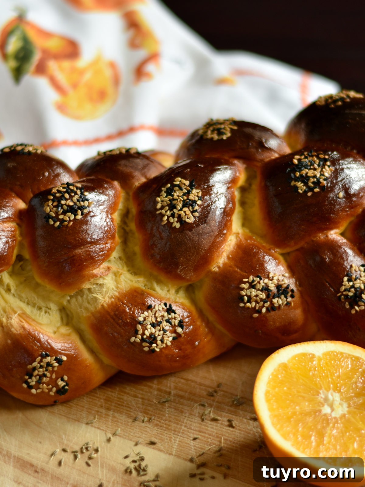 How to Braid Challah: Step-by-Step Visual Guide 8 Side view of a baked loaf of challah with seeds on it and an orange in the foreground.