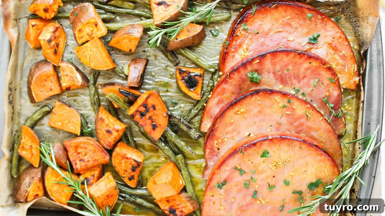 9 Ham Recipes Everyone Will Request Next Year 7 A baked dish with slices of glazed ham, roasted sweet potato cubes, and green beans, garnished with rosemary sprigs.