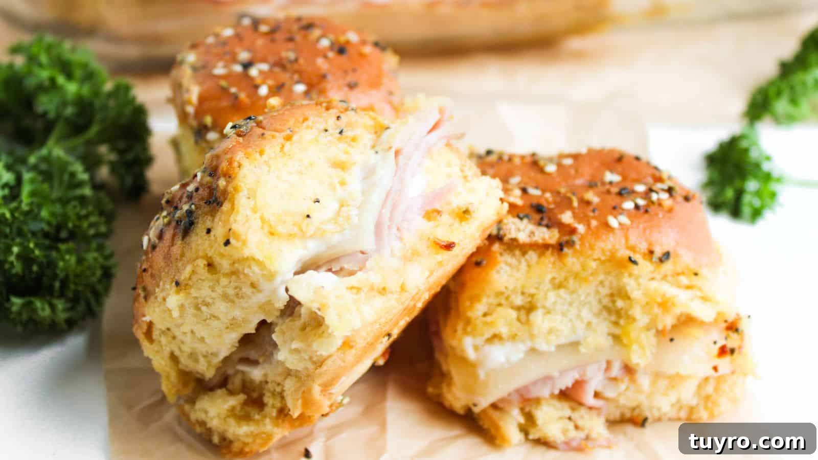 9 Ham Recipes Everyone Will Request Next Year 8 Three ham and cheese sliders on seeded buns are placed on parchment paper. Bright green parsley is visible in the background.