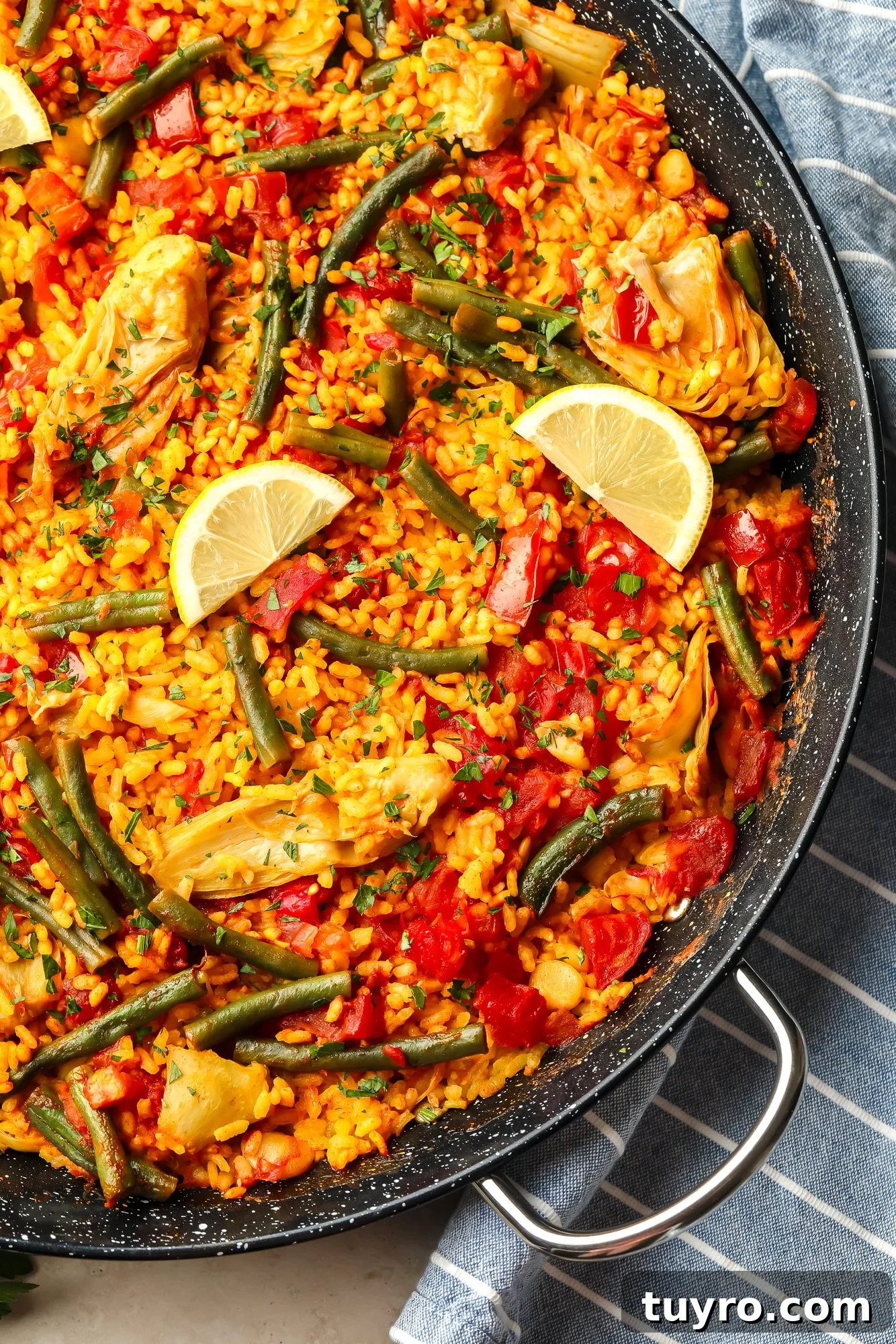 Vegan Paella with Saffron and Roasted Vegetables 2 vegan paella topped with lemon slices in a large black paella pan.