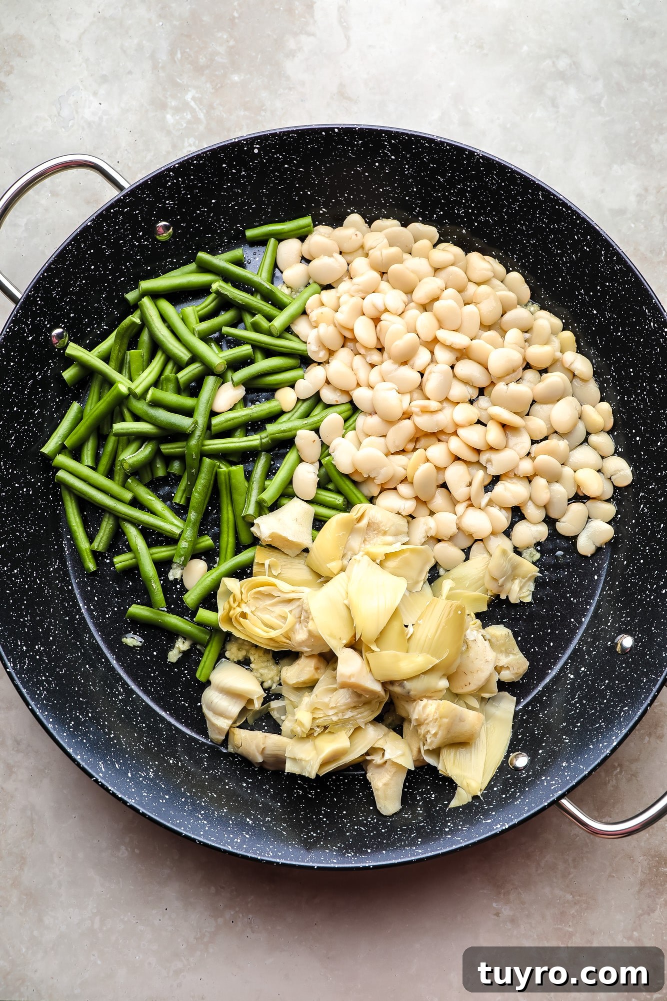 Vegan Paella with Saffron and Roasted Vegetables 3 green beans, artichoke hearts, and white beans in a large black paella pan.