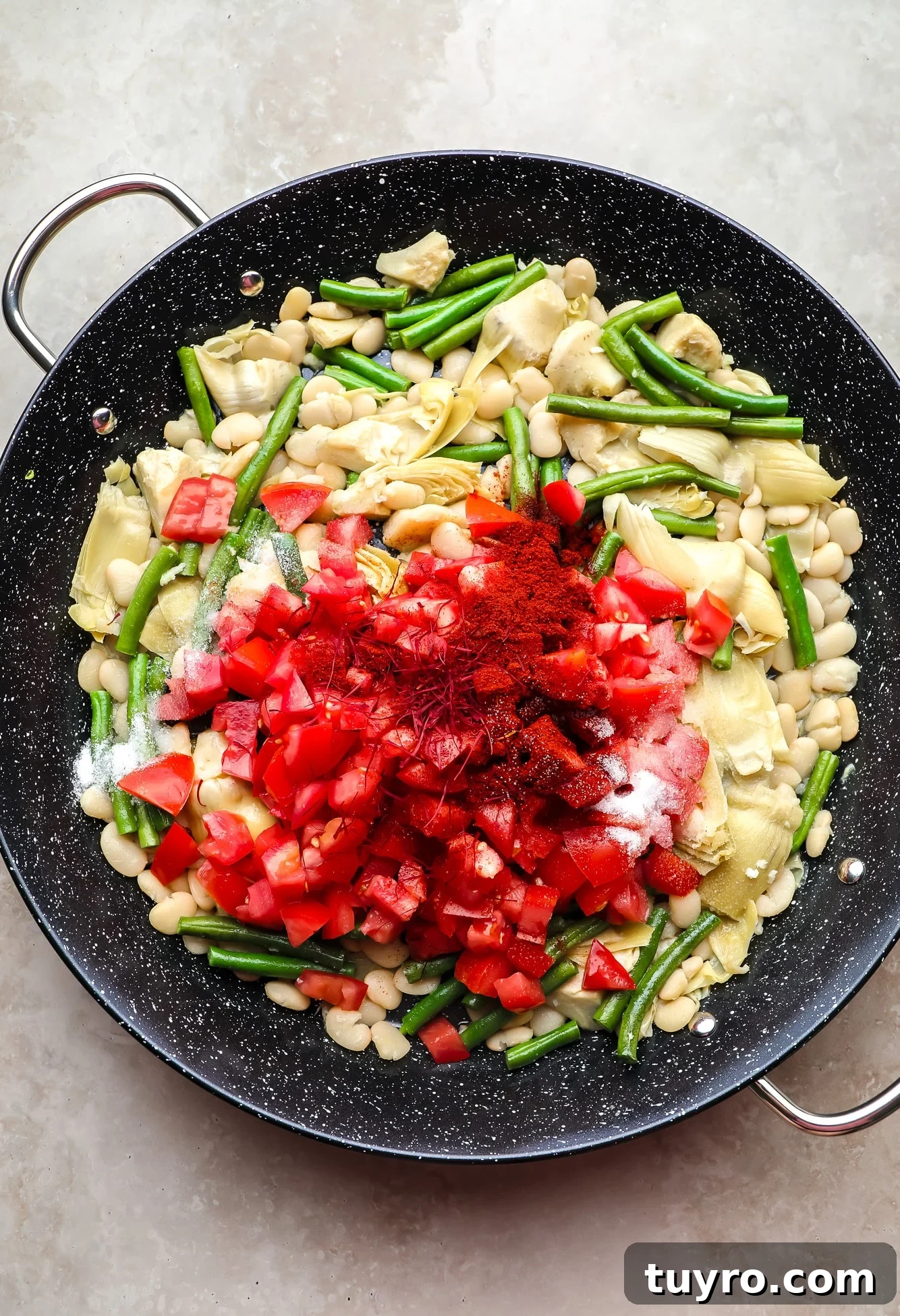 Vegan Paella with Saffron and Roasted Vegetables 4 chopped tomatoes and saffron on top of beans and artichoke hearts in a black paella pan.