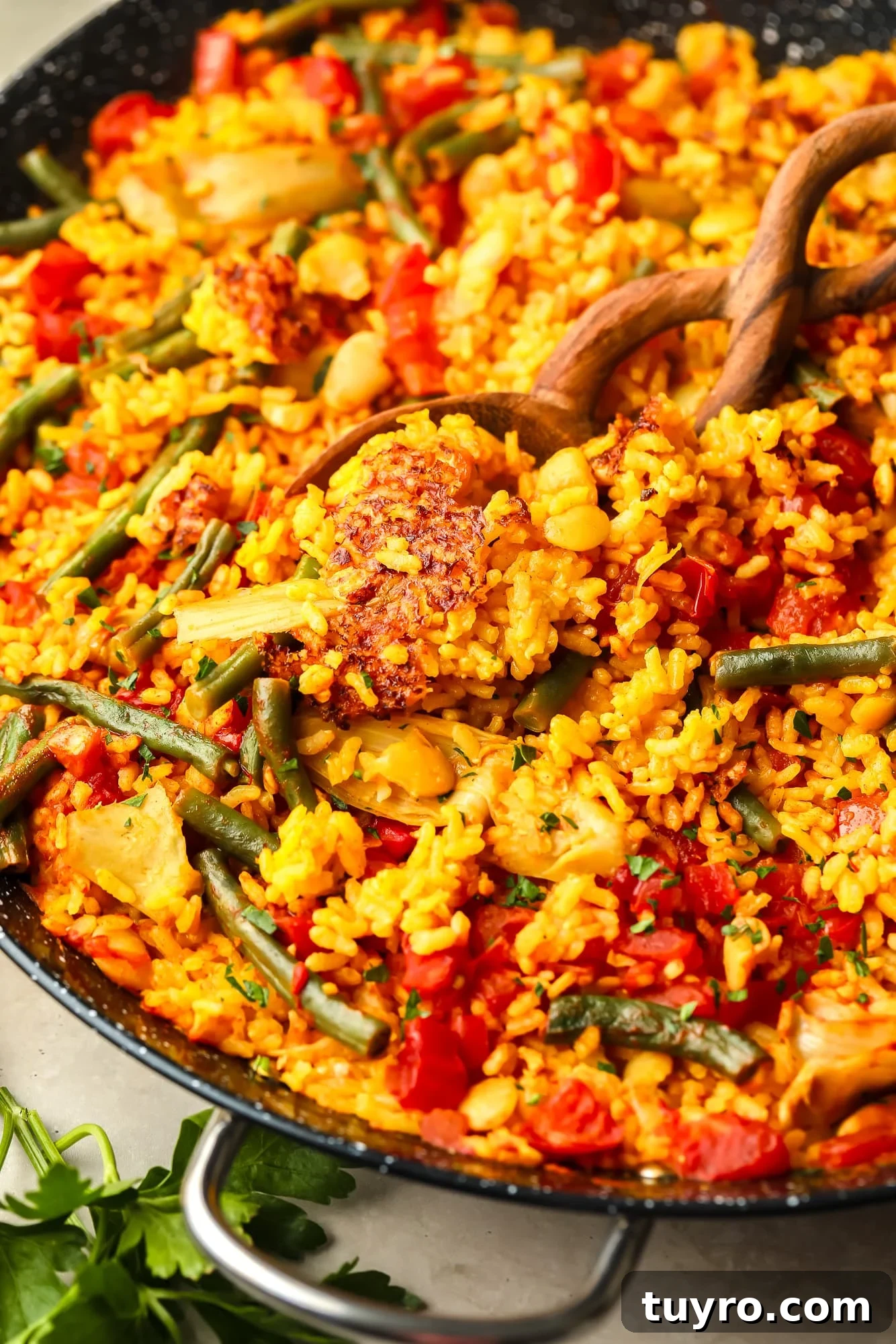 Vegan Paella with Saffron and Roasted Vegetables 6 a wooden spoon lifting a scoop of vegan paella out of a large black paella pan.