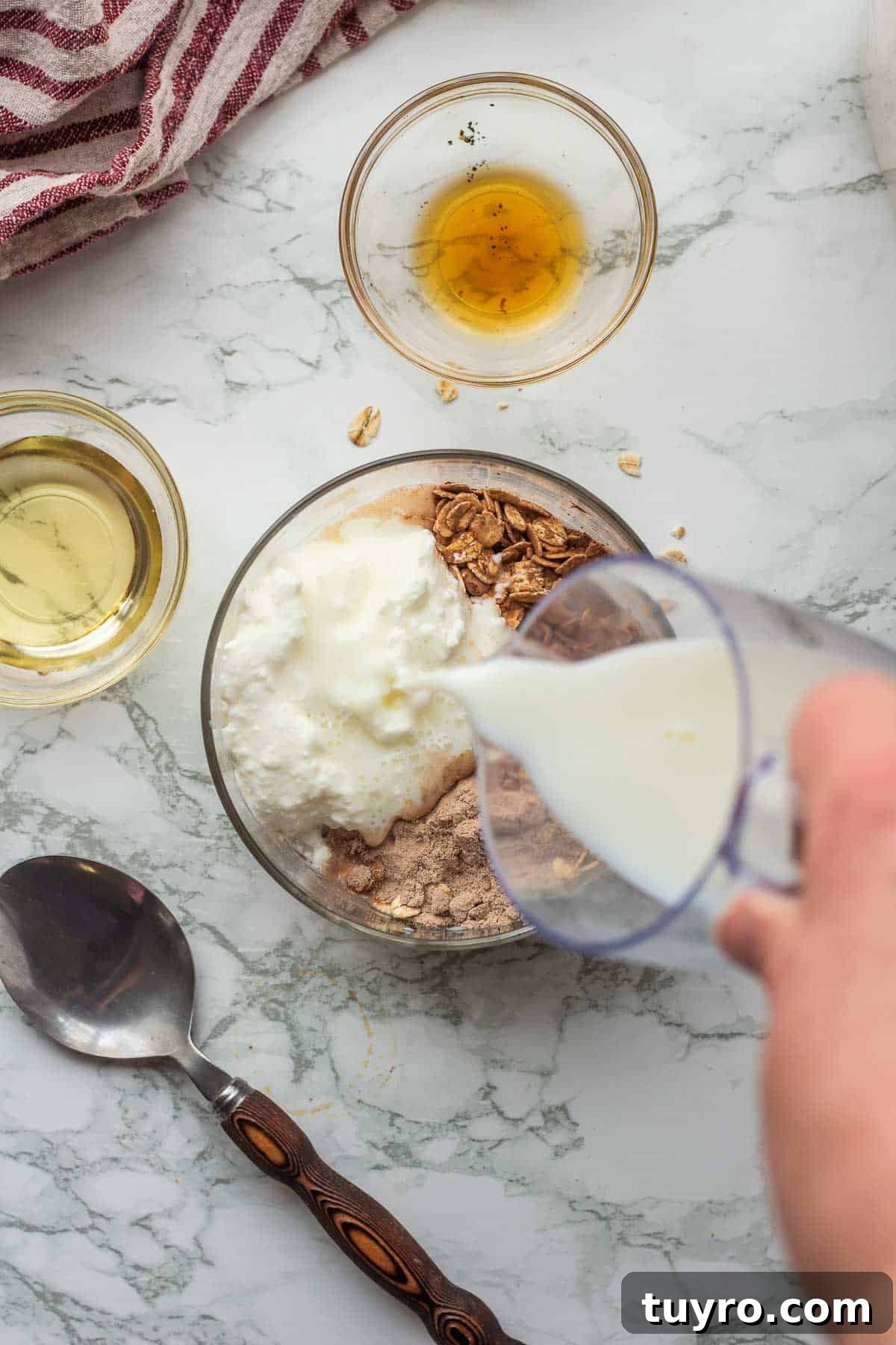 Brownie Batter Overnight Oats Recipe for Indulgent Breakfast 5 Pouring milk into glass bowl with oats, cocoa powder, protein powder, and greek yogurt.