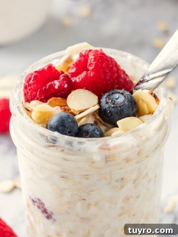 Jar of vanilla overnight oats topped almonds, raspberries and blueberries with metal spoon.