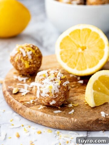 Lemon coconut protein ball on wood board with sliced lemon on marble backdrop.