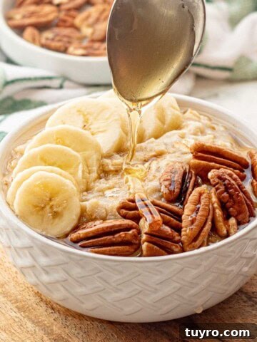 Spoon drizzling honey over white bowl of banana oatmeal.