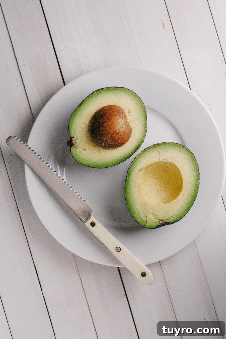 Two halves of an avocado on a white plate with knife