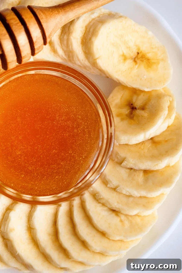 Slices of banana on a plate next to a small dish of honey