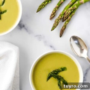 Creamy Asparagus Soup with Leeks and Peas 16 Two bowls of Creamy Asparagus, Leek and Pea Soup next to asparagus spears and a spoon.