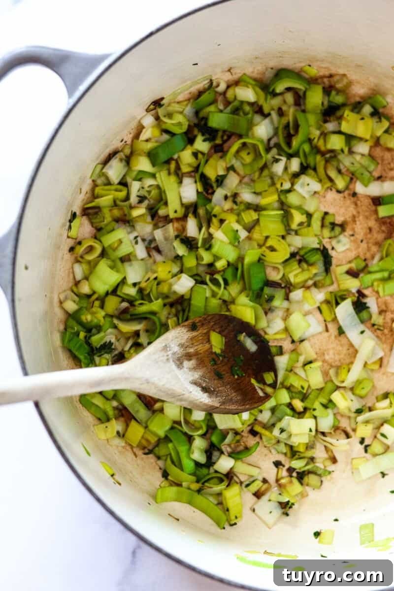 Creamy Asparagus Soup with Leeks and Peas 7 Leeks cooking in a pot with a wooden spoon.