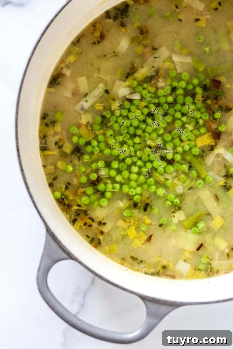 Creamy Asparagus Soup with Leeks and Peas 8 Soup in a pot with frozen peas on top.