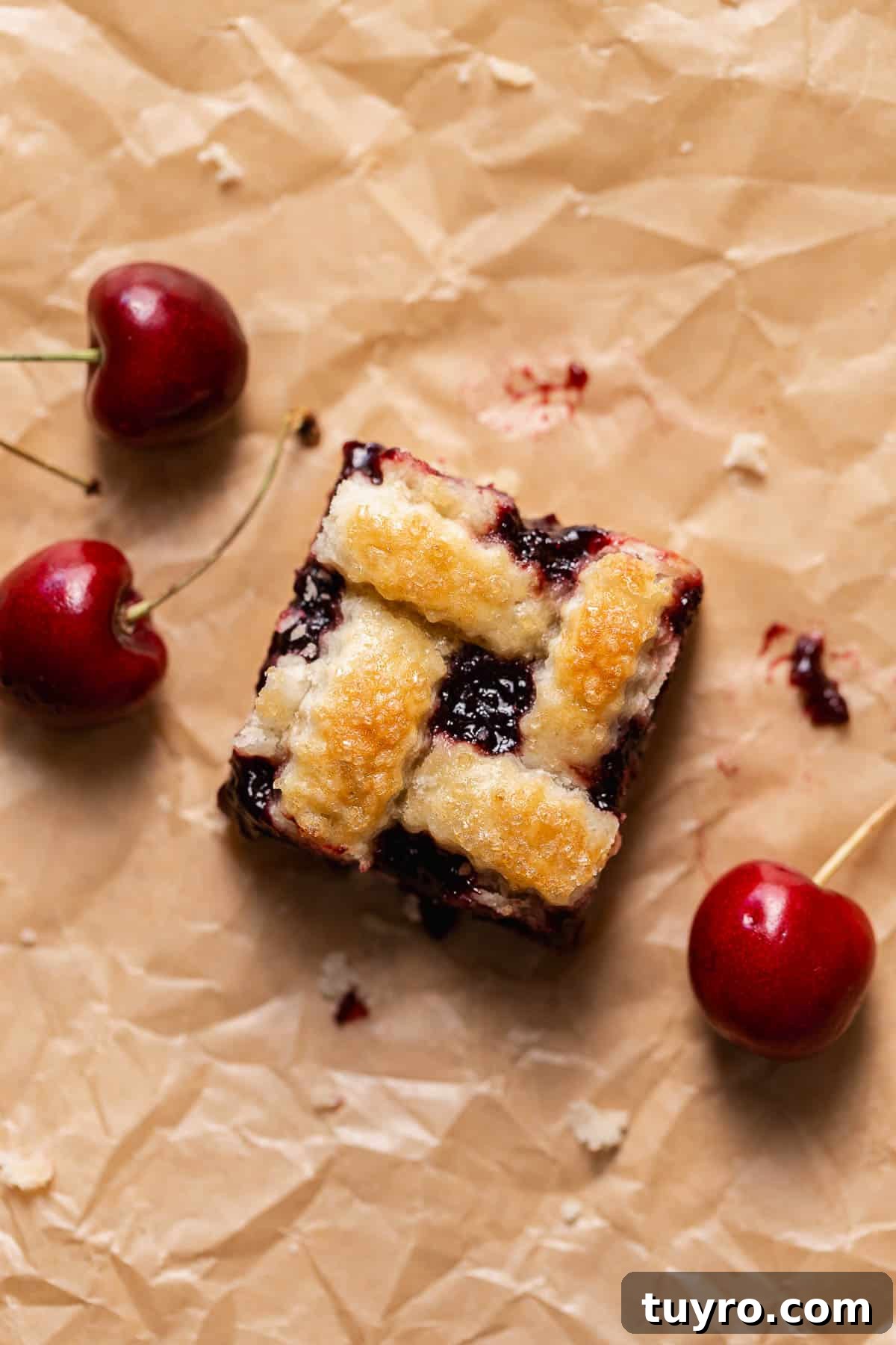Homemade Cherry Pie Bars with Buttery Crust 2 A cherry pie bar with pie crust on brown parchment paper with fresh cherries.