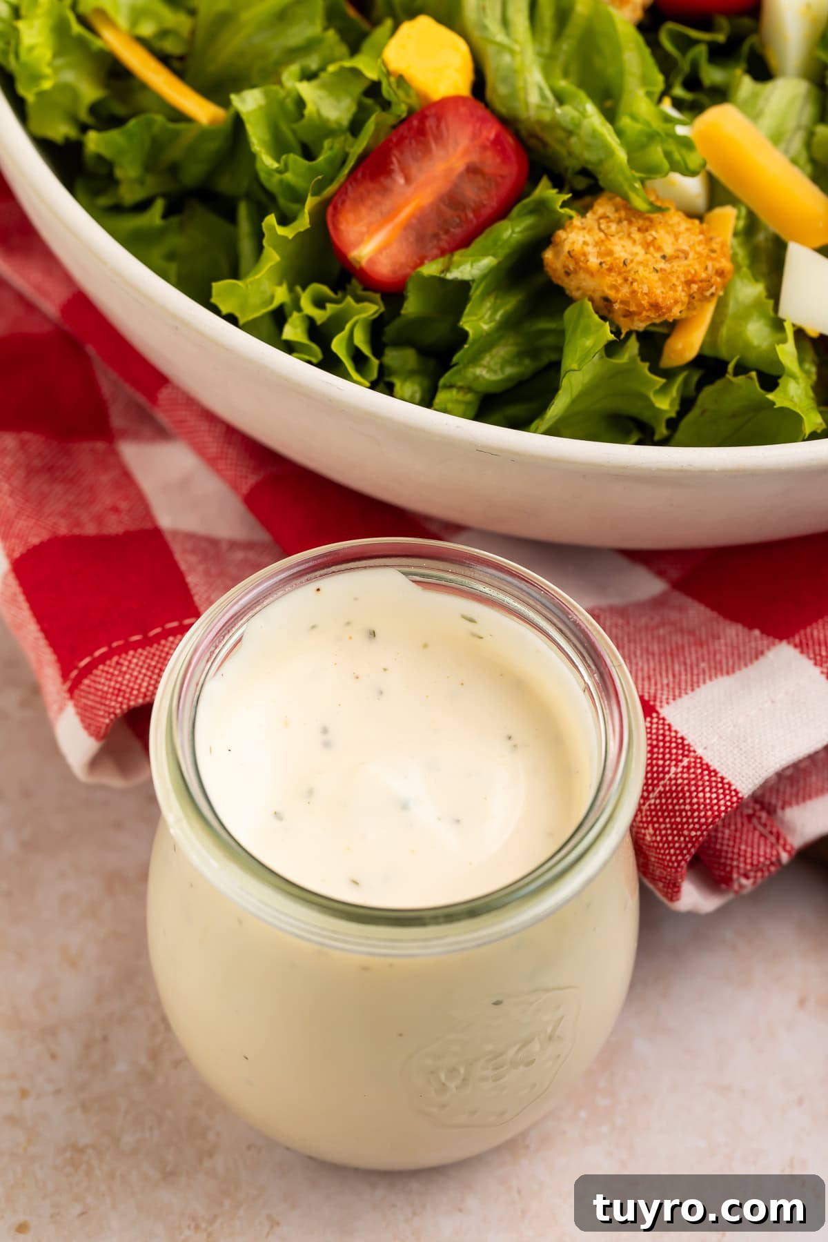 Glass jar of ranch dressing with a bowl of salad in the background.