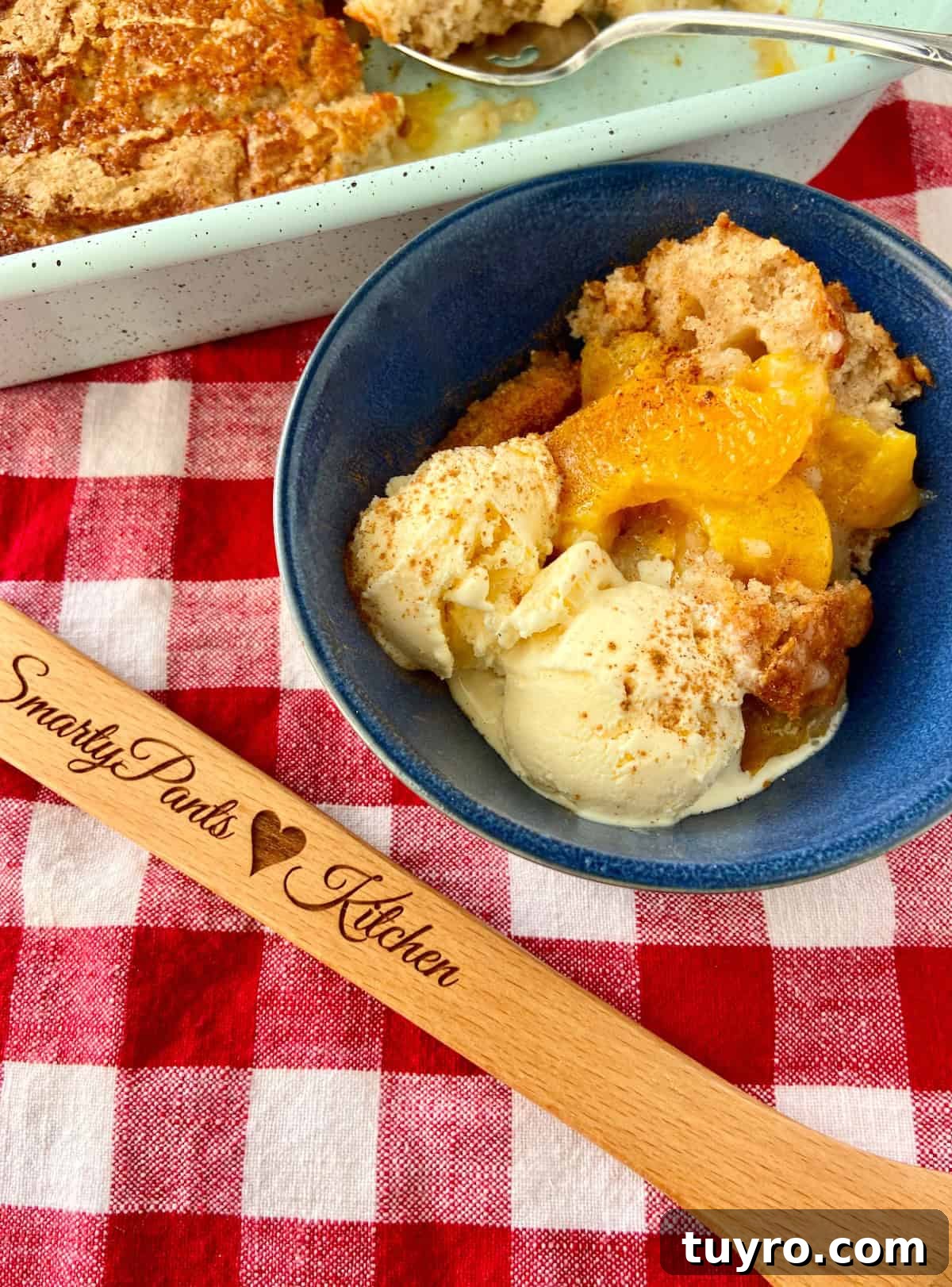 Classic Southern Peach Cobbler Recipe – Authentic & Irresistible 2 Peach cobbler in blue bowl on red and white checkered tablecloth.