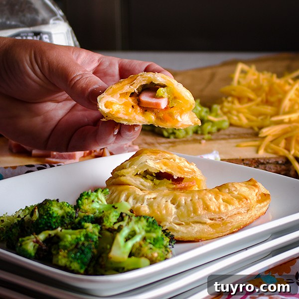 Holding up a piece of a ham and cheese hand pie so you can see the filling inside of the pastry.