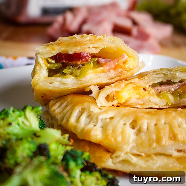 Two ham and cheese hand pies on a plate, one broken open to see the filling.