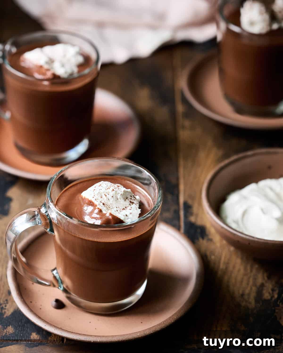 Creamy Vegan Hot Chocolate Recipe 2 Three glass mugs filled with hot chocolate and whipped cream on plates on a wood table.