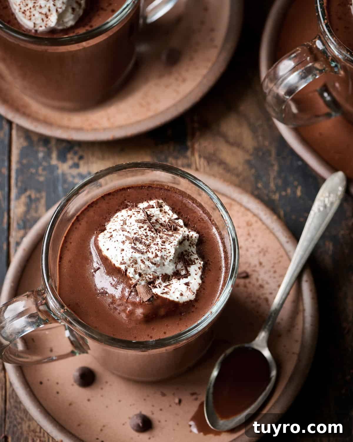 Creamy Vegan Hot Chocolate Recipe 13 Overhead view of three mugs of hot chocolate with whipped cream on a plate on a wood table.