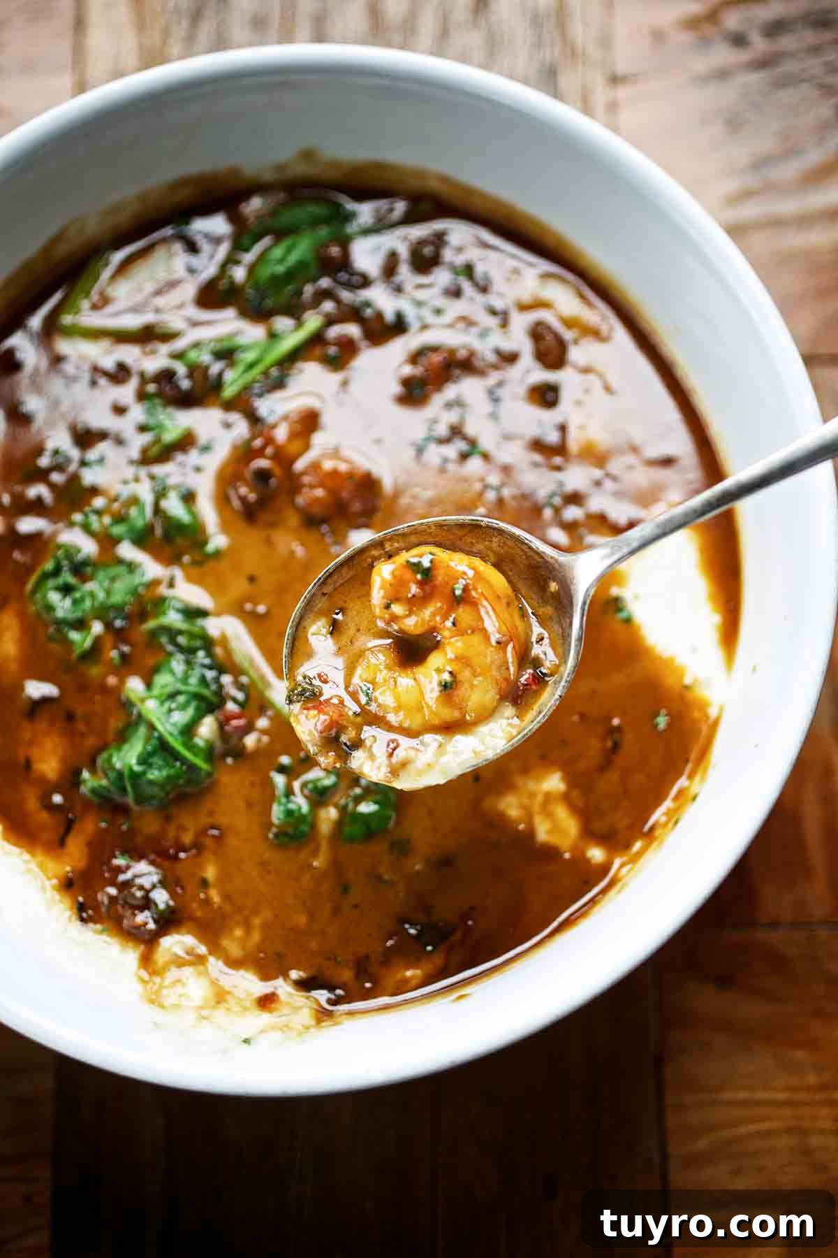Creole Shrimp and Grits Recipe — Bold Southern Flavor in 30 Minutes 2 A white bowl filled with Creole shrimp and grits, with a spoon above the bowl with a shrimp in it.