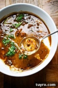 Creole shrimp and grits in a white bowl, with a spoon above the bowl with a shrimp in it.