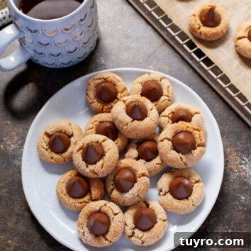 Chewy Peanut Butter Blossom Cookies with Chocolate Kiss 3 Peanut Butter Cookies topped with a Hershey Kiss sit on a off-white plate next to a cup of coffee.