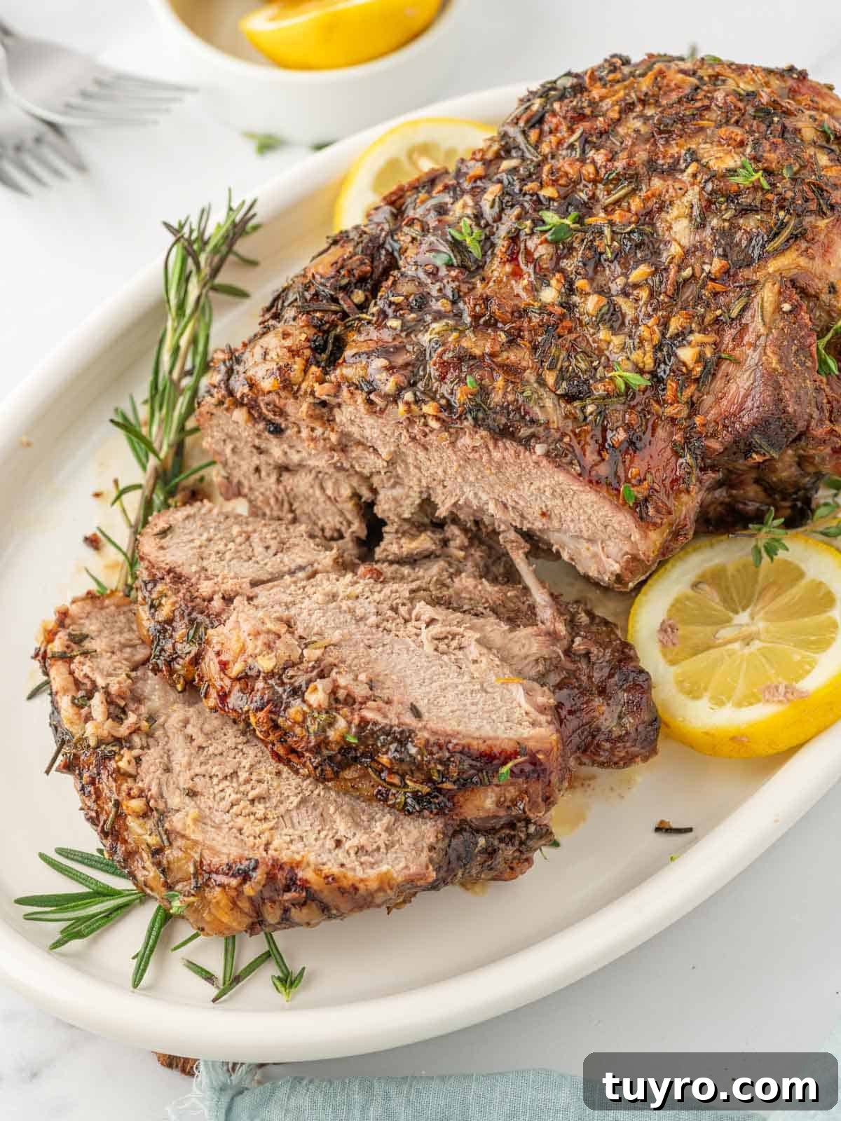 Boneless Leg of Lamb Roast Recipe: Tender, Juicy, Oven-Roasted 2 Leg of lamb with slices cut garnished with lemon and rosemary.