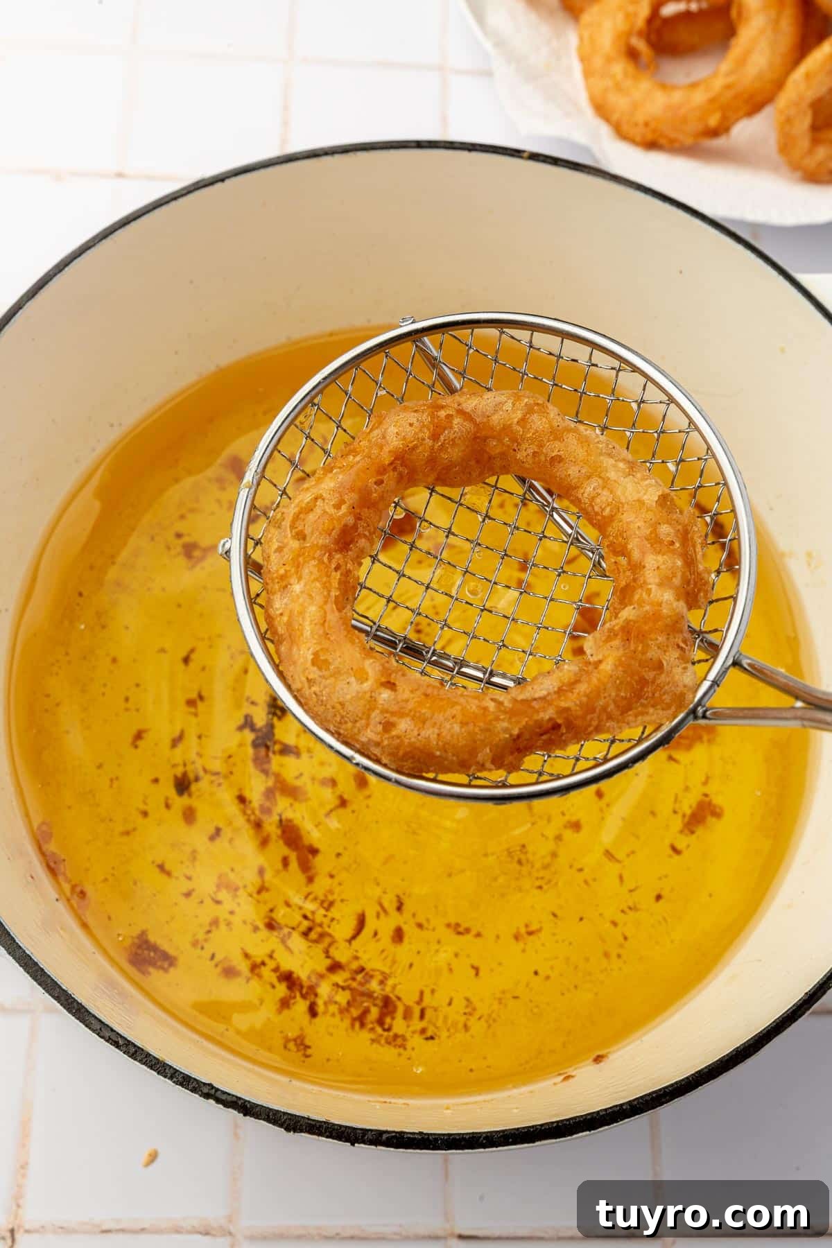 Crispy Gluten-Free Onion Rings Recipe 11 A wire spider spatula removing a gluten free onion ring from a pot of hot oil.