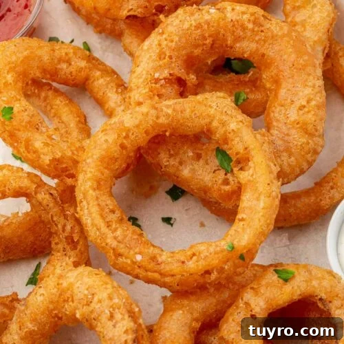 Crispy Gluten-Free Onion Rings Recipe 14 A close up of gluten free onion rings topped with parsley on a parchment lined baking sheet with ketchup peaking in.