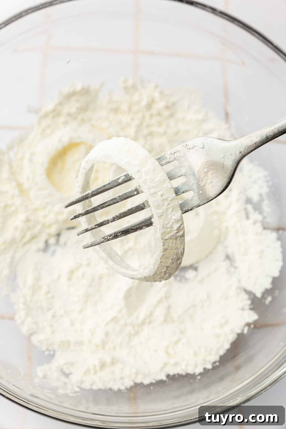 Crispy Gluten-Free Onion Rings Recipe 9 A cornstarch dipped onion ring on a fork over a bowl of additional cornstarch.