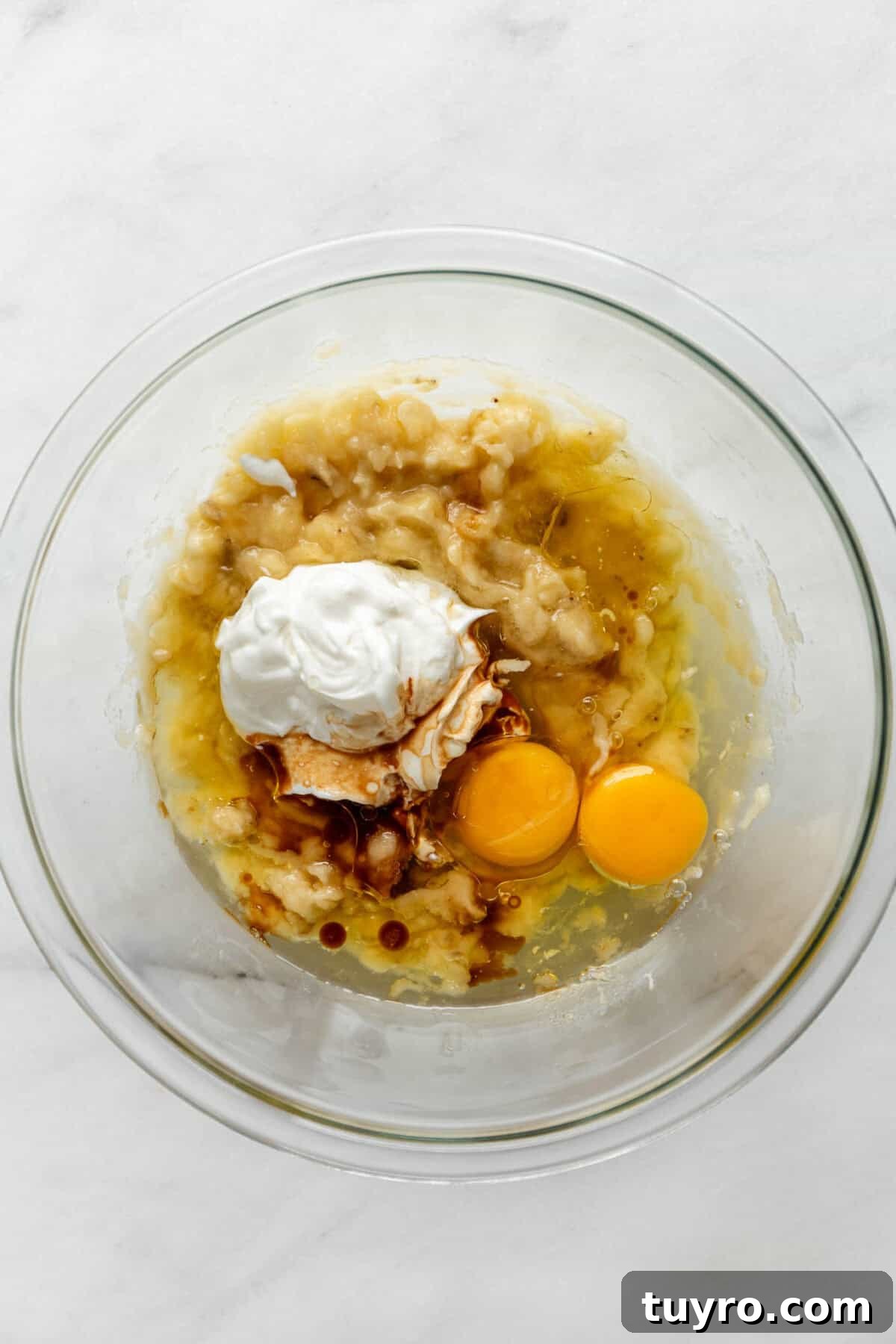 High-Protein Banana Muffins for Quick Breakfast and Snacks 4 mashed banana, eggs and greek yogurt in a clear mixing bowl.