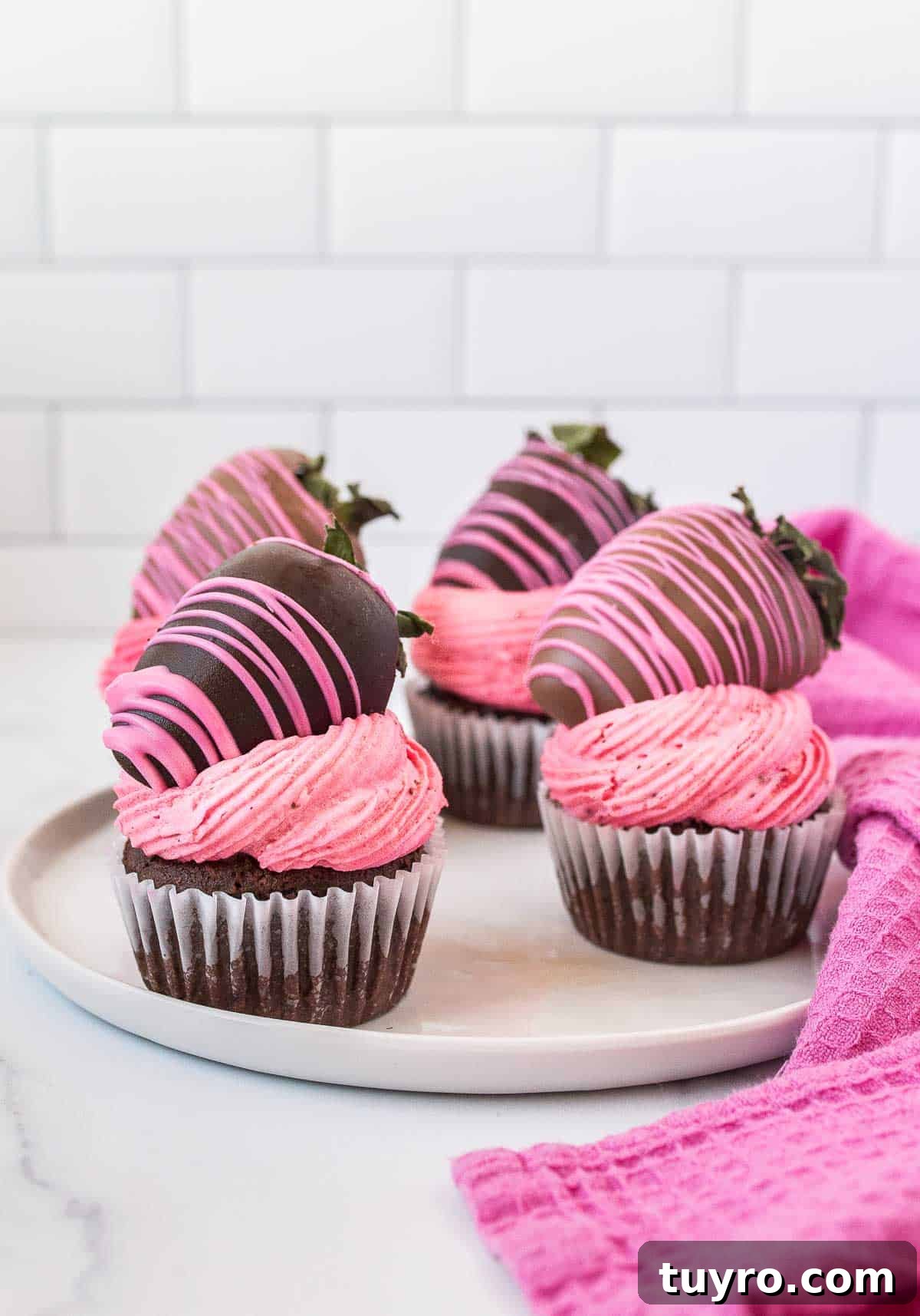 plate of chocolate cupcakes with pink frosting and chocolate covered strawberries on top.