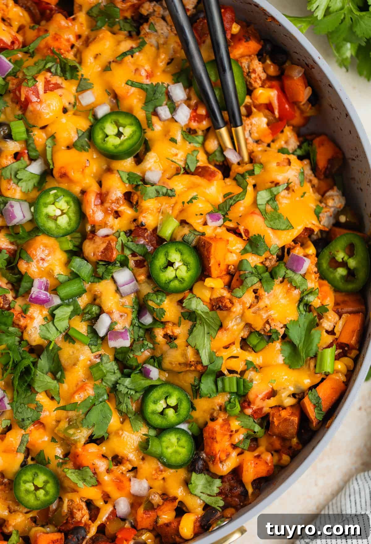 Skillet with ground turkey and sweet potatoes topped with melted cheese and serving utensils scooping in.