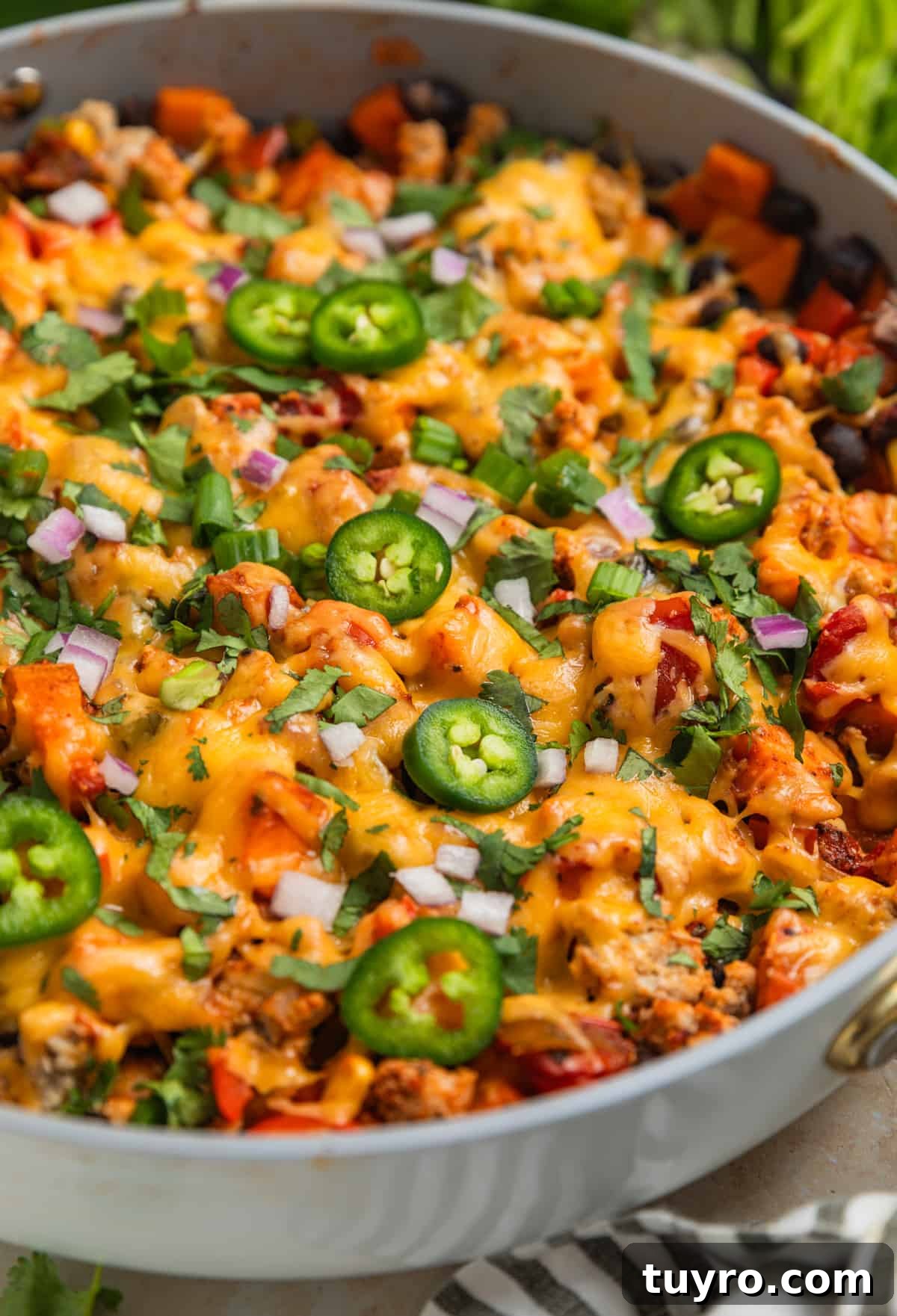 Skillet with cooked meat and vegetables topped with melted cheese, cilantro, peppers, onions and more.