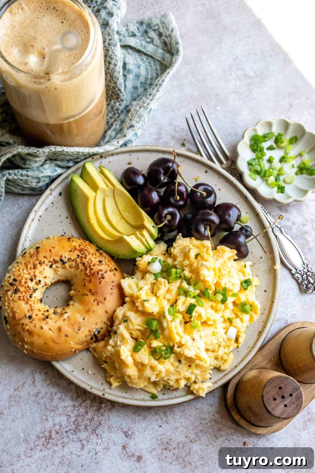 A ceramic plate with Cottage Cheese with Scrambled Eggs on it and a bagel to the side.