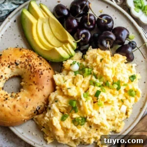 Cottage cheese scrambled eggs on a plate with a bagel, sliced avocado, and cherries.