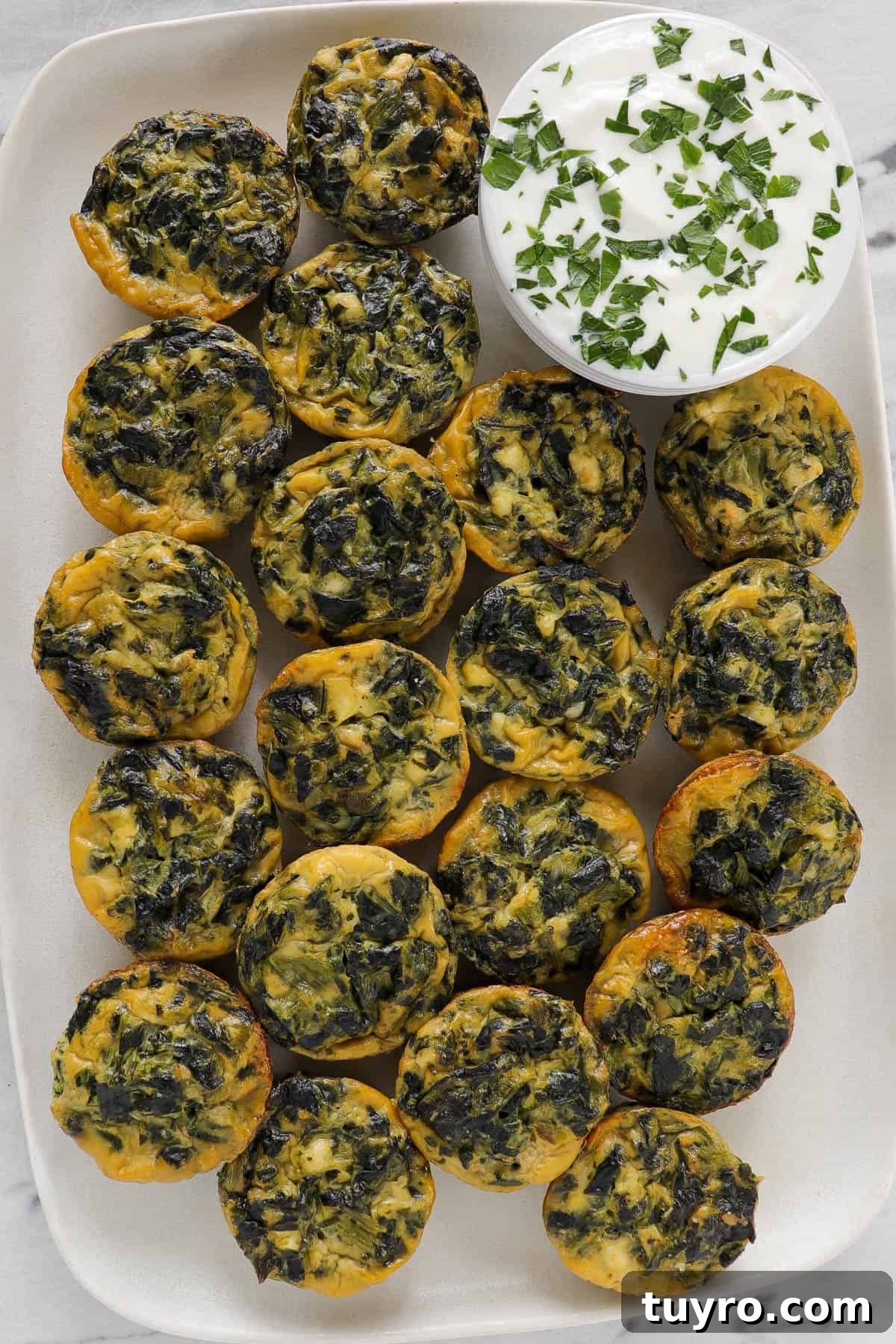 Mini spinach and feta quiche on platter with yoghurt topping sauce.