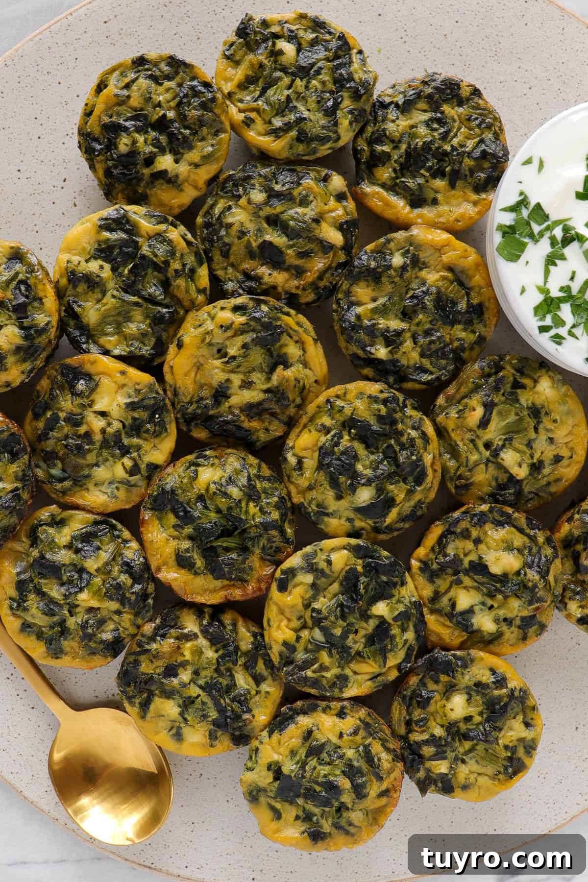 Mini spinach and feta quiche on big plate with yoghurt topping sauce and gold spoon for decoration.