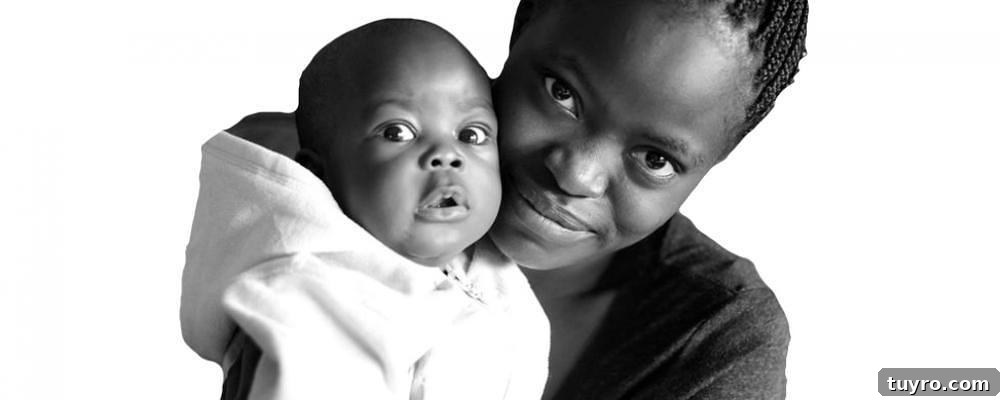 Image shows a woman holding a small baby in a hooded onesie. Both are looking at the camera.