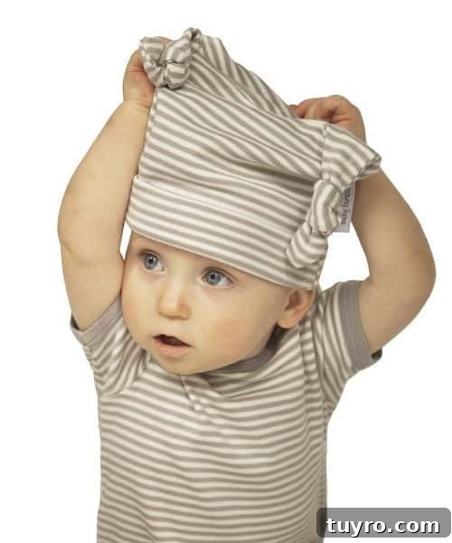 Image shows a baby in a striped shirt and hat pulling the hat off its head with both hands