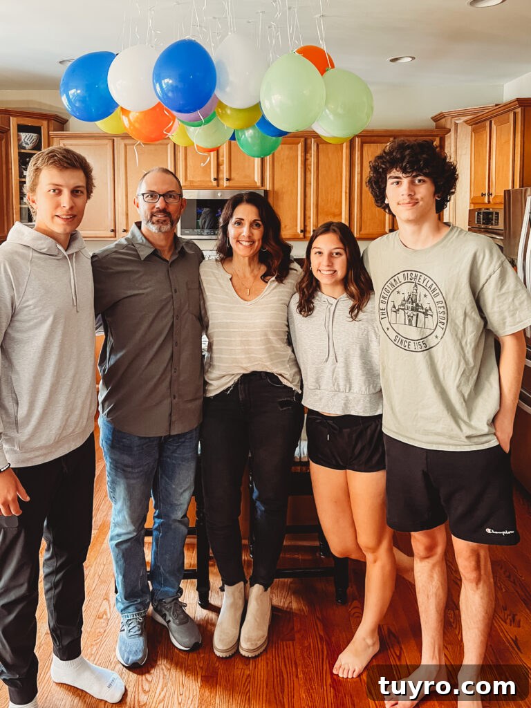 30+ Activities to Connect with Your Young Adult Children 19 Family standing together in the kitchen under colorful balloons, celebrating a birthday with young adult children at home.