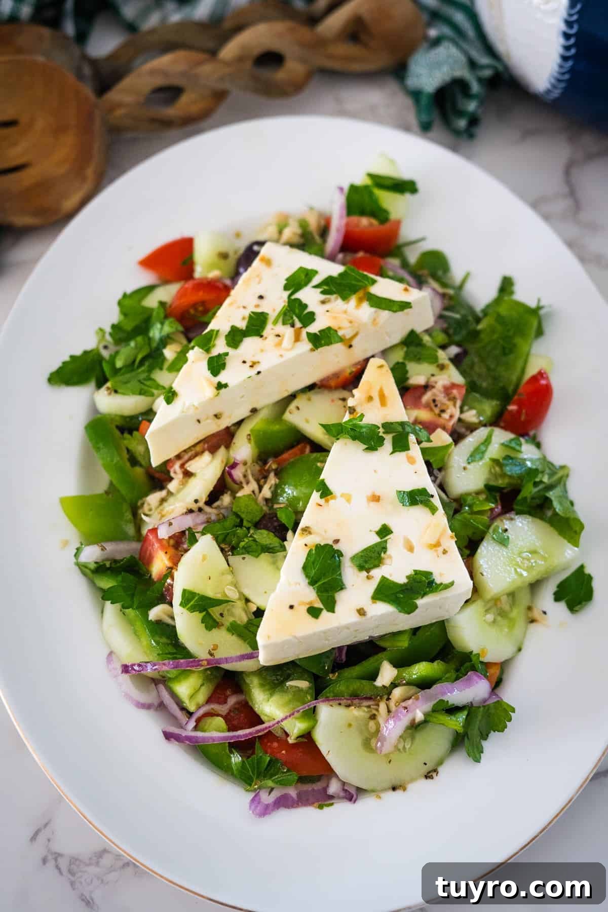 Authentic Greek Horiatiki Salad Recipe — Classic Village Salad 9 A white plate filled with a fresh Greek village salad featuring cucumber, tomato, red onion, green pepper, herbs, and two large wedges of cheese on top.